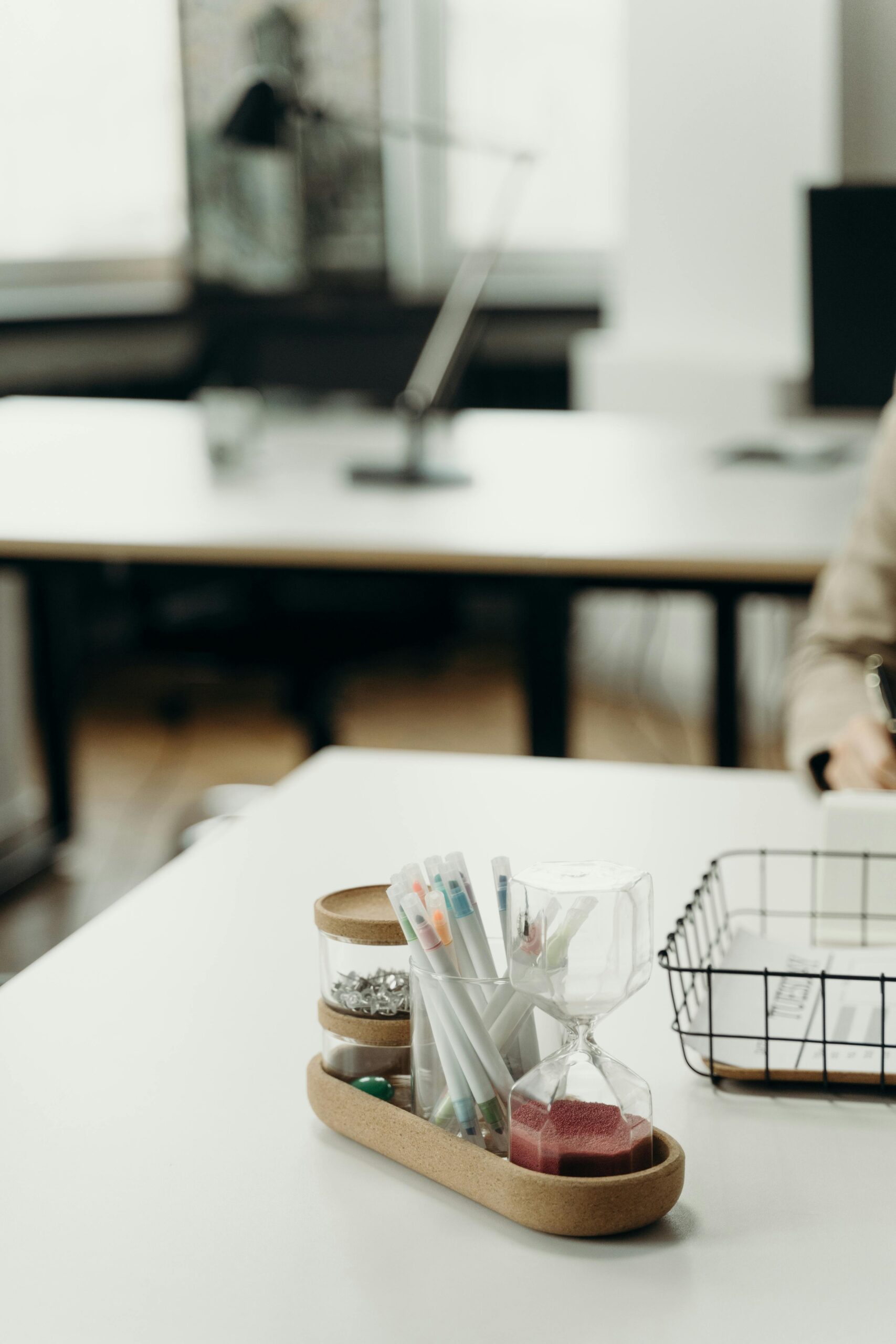 A neatly organized office desk featuring a tray with markers, an hourglass, and paperclips.